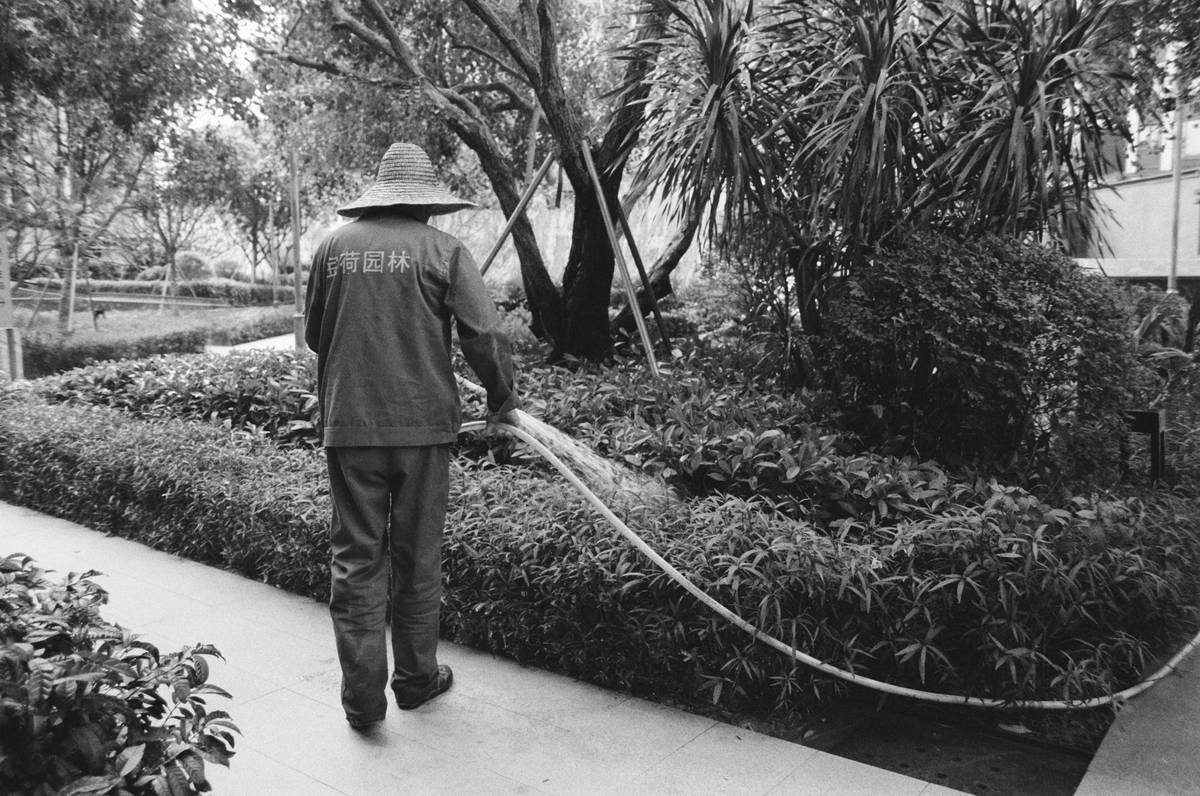 Three common garden hose sprayer types displayed on a wooden garden bench: adjustable, pistol grip, and soaker nozzle.